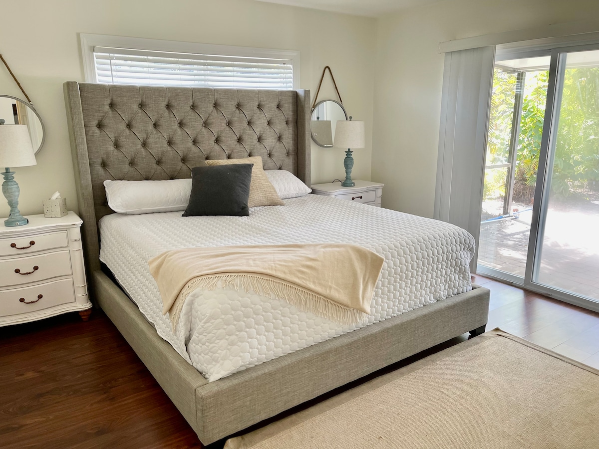 Dormitorio principal con cama tamaño king, salida al área de la piscina, baño completo adjunto, TV montada en la pared y ventilador de techo.