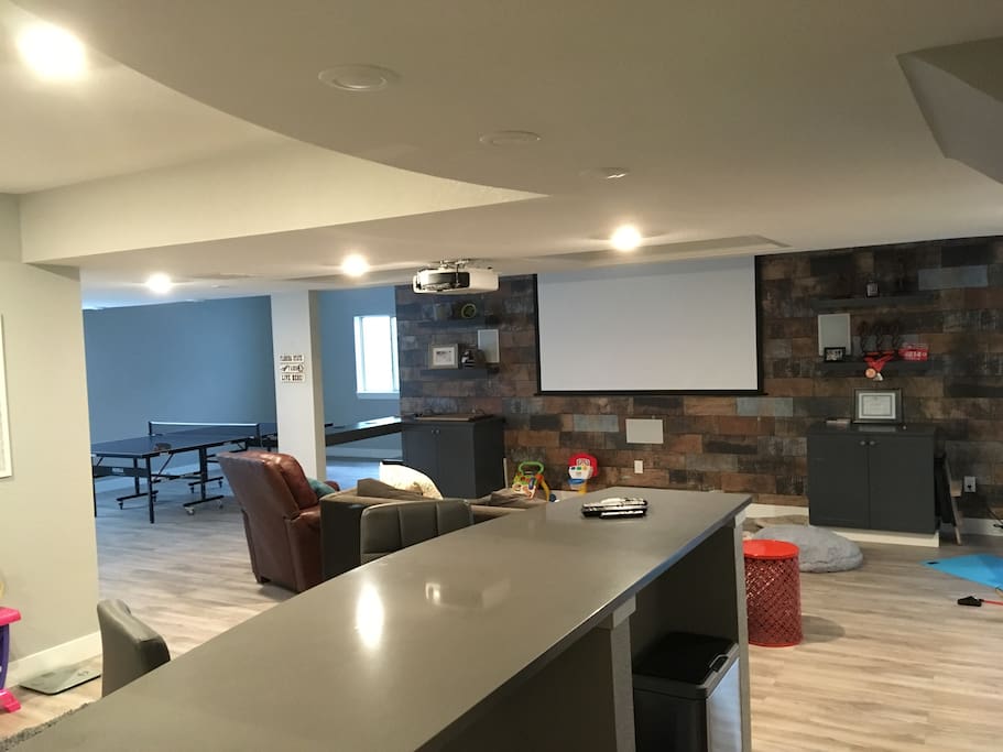 Basement area with projection screen, living area and bar (desk space) with sink and small refrigerator