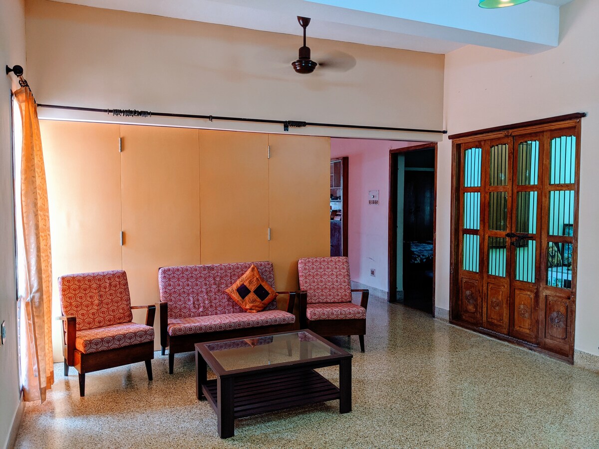 A spacious living area is presented with a glass coffee table positioned at the center. Four comfortable chairs are arranged around it, complemented by an accent pillow on one chair. A folding partition is visible, along with decorative wooden cabinets that enhance the overall ambiance.