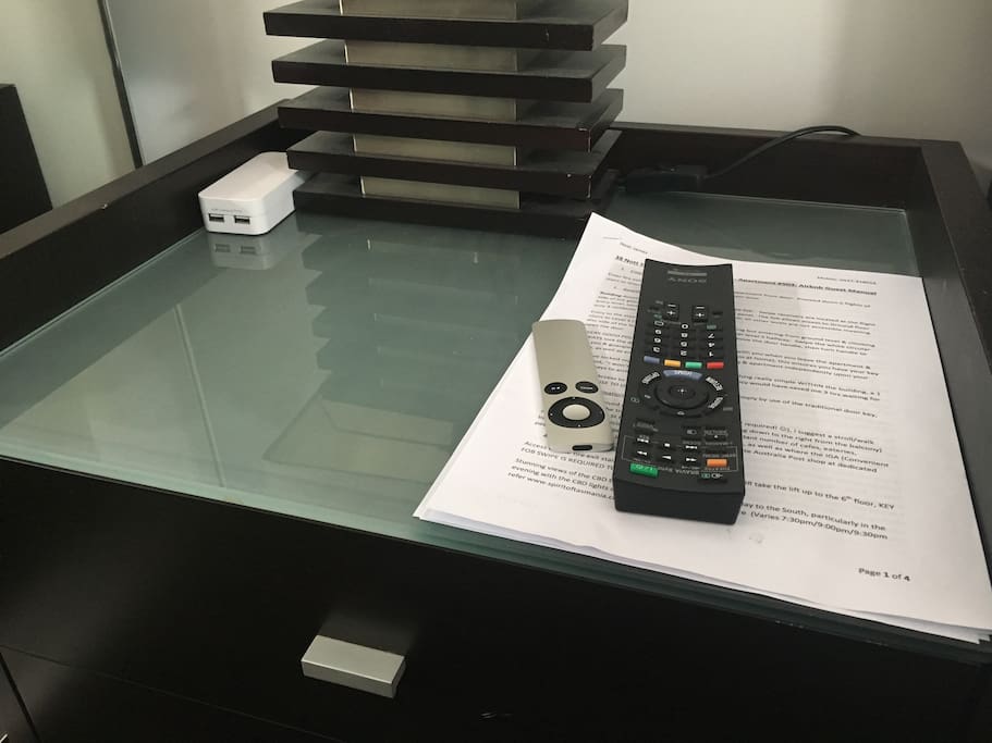 Bedside table with TV remotes, guest manual & USB power station for wash device charging.