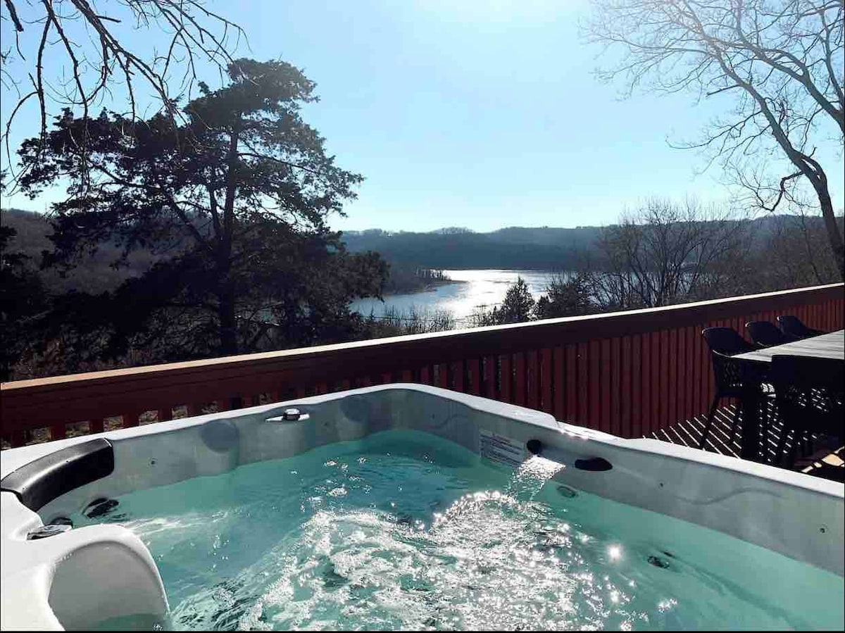 A hot tub sits on an outdoor deck, surrounded by peaceful natural scenery. The sparkling water reflects sunlight, with views of Center Hill Lake and wooded hills in the background, creating a serene atmosphere for relaxation.