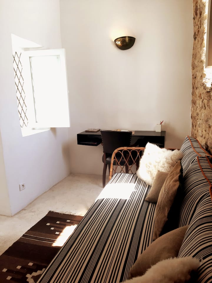 Malá obývacia izba s písacím stolom a pohovkou, ktorá môže slúžiť ako samostatná posteľ