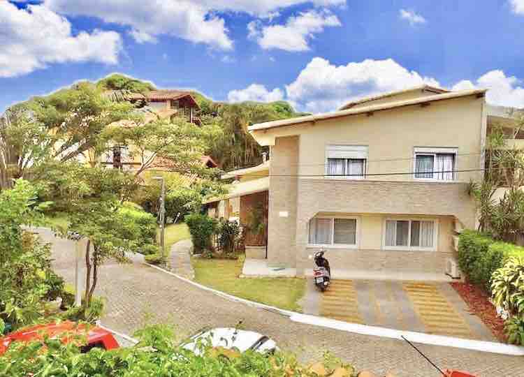 The exterior of a charming two-story house is showcased, surrounded by well-maintained greenery. A paved pathway leads to the entrance, with nearby residences visible in the background. The sky is filled with clouds, providing a lovely backdrop to the peaceful neighborhood setting.