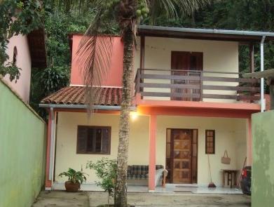 The two-story building features a coral-painted façade with a tiled roof. A palm tree stands in the foreground, while wooden doors and windows provide an inviting entrance. A small porch area is visible, promoting outdoor relaxation.