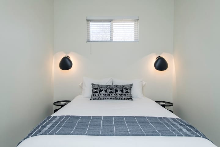 Bedroom area with sconce lighting, ceiling fan/light, fuzzy bedside rugs, cotton bedding and Dohm sound machine.