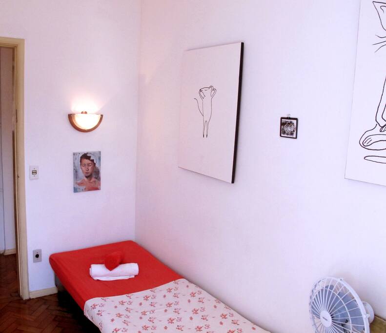 Quarto de solteiro com cama, TV simples, armário e ventilador.