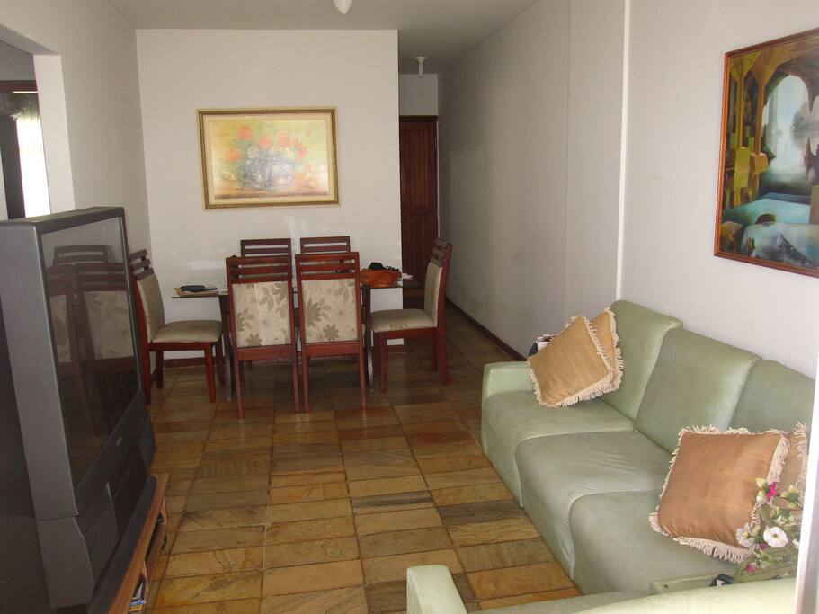 Vista da sala com Tv, sofa e mesa de jantar.