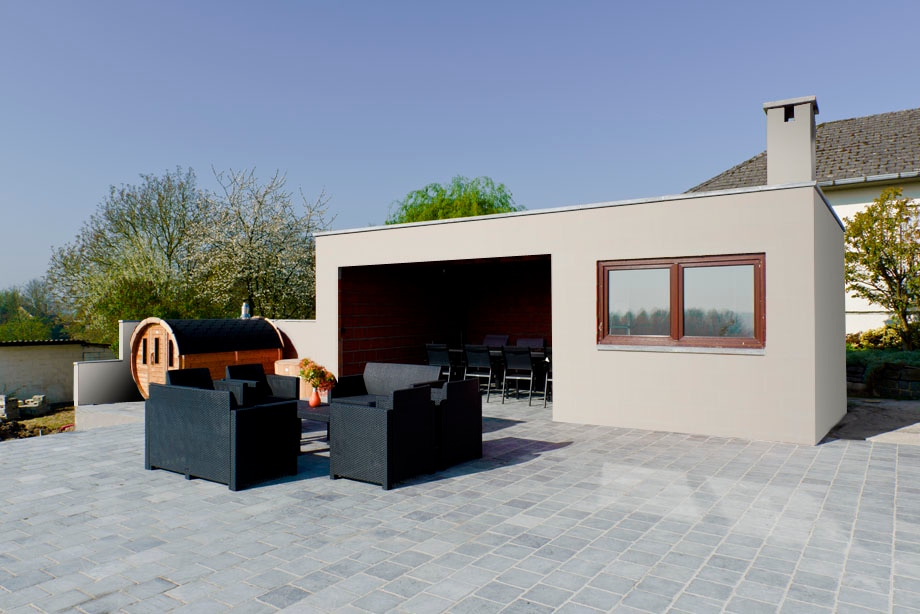 An outdoor seating area features dark wicker furniture arranged around a stone-paved patio. A wooden sauna is positioned to one side, while a large window provides views of the surroundings. Lush greenery is visible in the background, enhancing the outdoor setting.