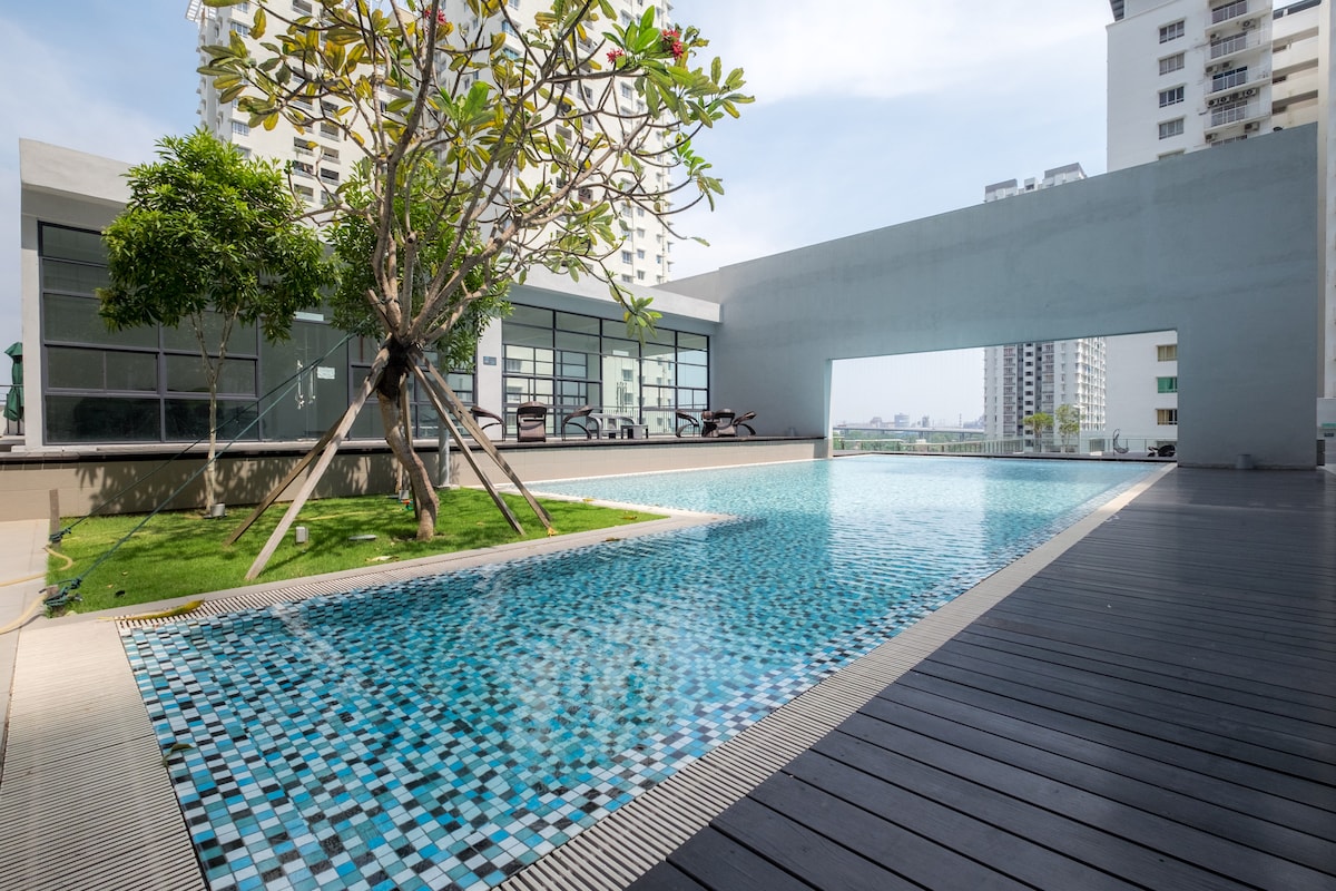 A shimmering swimming pool captures attention with its mosaic tile design, surrounded by well-maintained greenery. Lounge chairs are positioned next to the water, inviting relaxation under the warm sun, while an expansive area of wooden decking enhances the outdoor space.