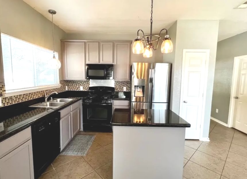 The kitchen features granite countertops and modern appliances, including a refrigerator and a stove. Ample cabinetry is present for storage, and a large window allows natural light to fill the space. Pendant lighting adds a warm touch, complementing the neutral wall colors.