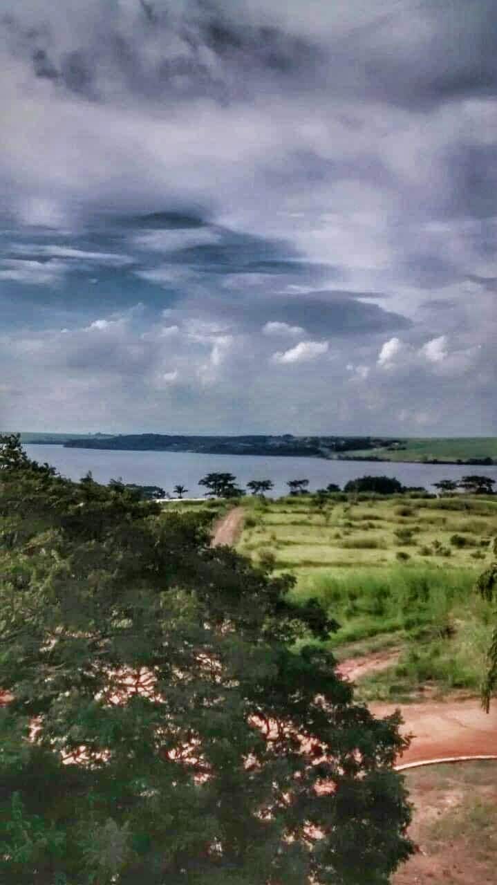 A scenic view of a lake is presented in the distance, with lush greenery and a dirt path leading to the water's edge. Wispy clouds fill the sky, enhancing the peaceful atmosphere of the surroundings.
