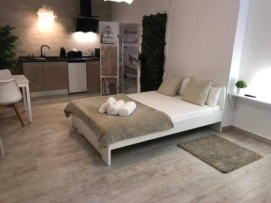 Vista de la cama del estudio, al fondo la cocina y a la izquierda una mesa para poder desayunar, comer o cenar.