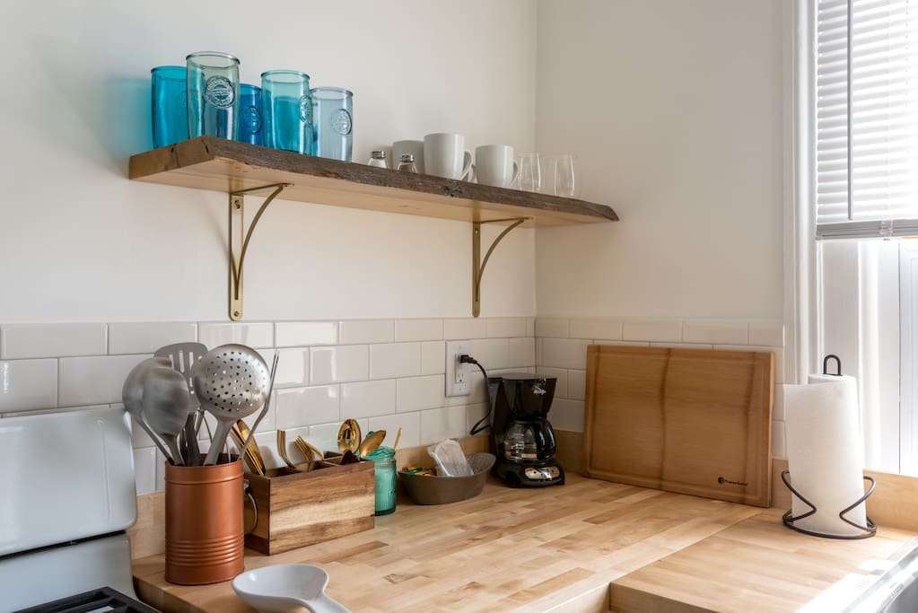 Well-stocked with blue-green glassware and gold flatware. Custom-built live-edge wood shelving!