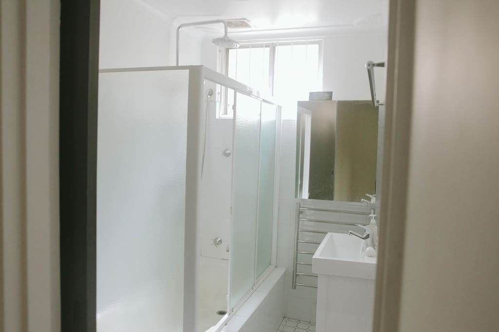 Bathroom, showers are in the bath. A tall shower & there is a hand held shower, heated towel rack, mirrored vanity & sink. The toilet is to the left of shower screen. The bath is not very high, but you do have to climb in to use the shower.