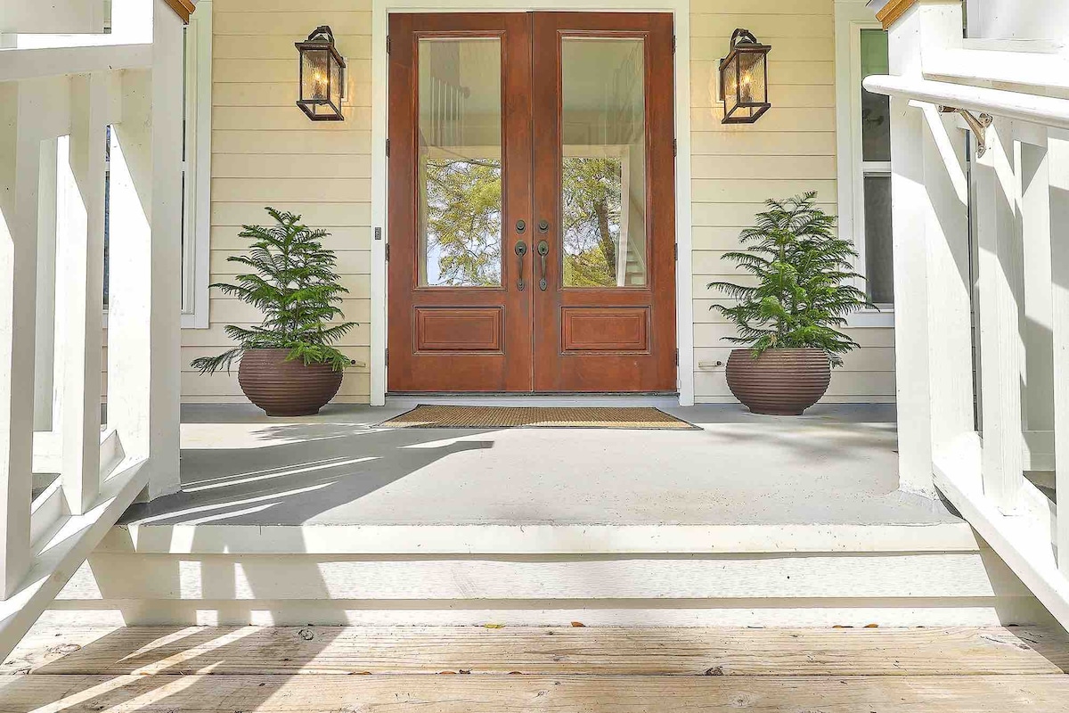 A welcoming entrance is showcased with double wooden doors framed by two lanterns. Potted ferns add a touch of greenery to the porch, while the light-colored steps lead up to the entryway.
