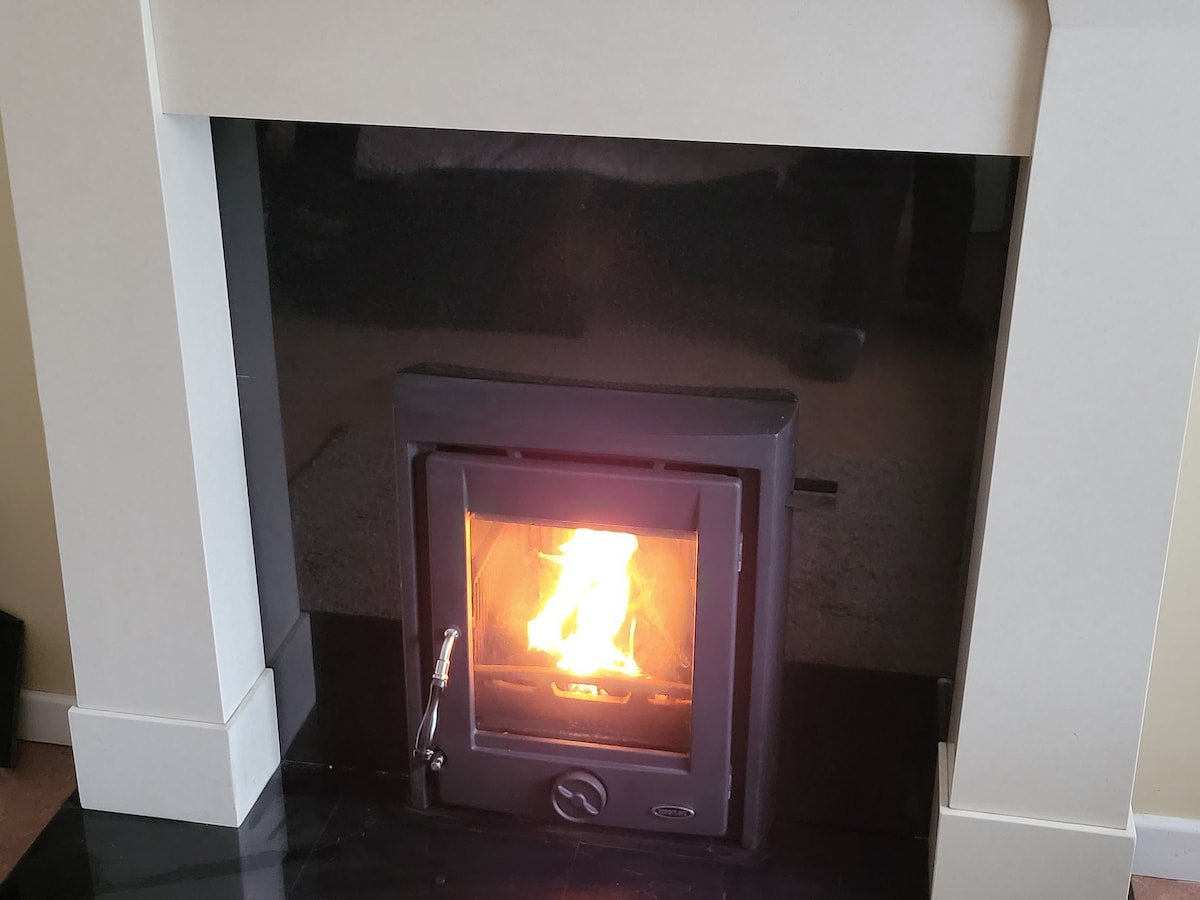 A modern fireplace is centered in a sleek mantel. The flames flicker softly within a black frame, providing warmth and light to the surroundings. The hearth is finished in dark stone, complementing the clean lines of the fireplace design.