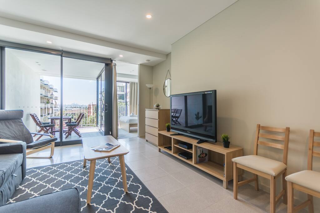 Bright living room with 3 seater sofa bed (queen), comfortable chair, huge TV with Optus Fetch (cable TV) & Netflix for guests! There is also a DVD player. Glimpses of the city you can see from here!