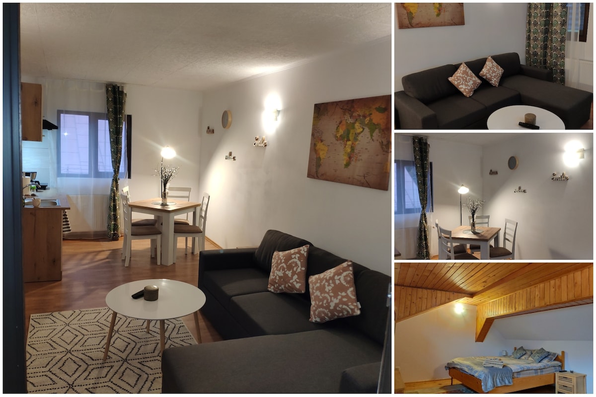 An open living area displays a dark sofa accented with patterned cushions, paired with a white coffee table. A wooden dining table and chairs are positioned nearby, under soft lighting. A cozy bedroom with a sloped ceiling features a relaxed sleeping area with a casual bedding arrangement.