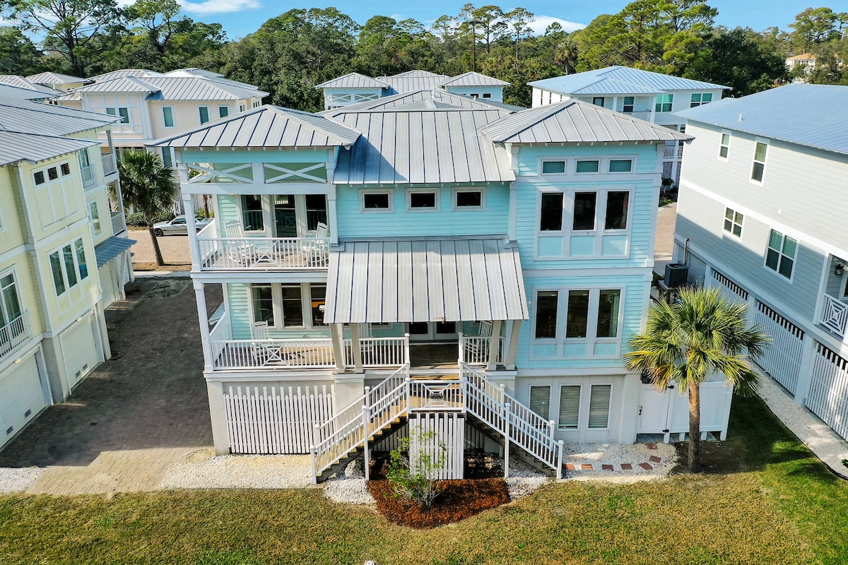 The exterior of a modern two-story home is showcased, complemented by a metal roof and large windows. A welcoming front porch leads to multiple entry points, while surrounding greenery and a neatly paved pathway enhance the inviting appearance of the property.