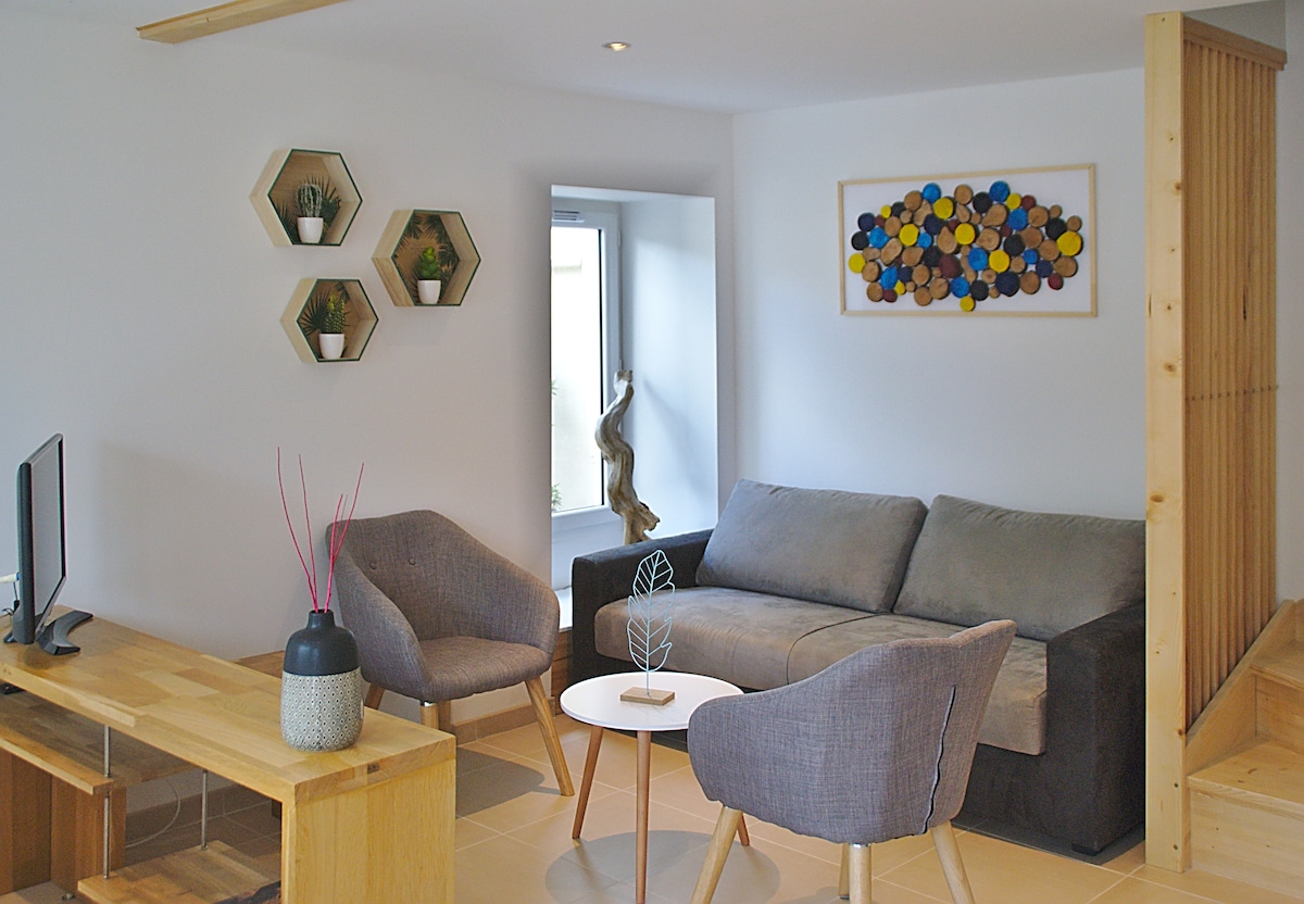 A modern living area features a gray sofa and two armchairs, creating a comfortable seating arrangement. A wooden coffee table sits in the center, accented by a decorative vase. Walls display geometric wall art and simple plant decor, enhancing the clean, minimalist space.