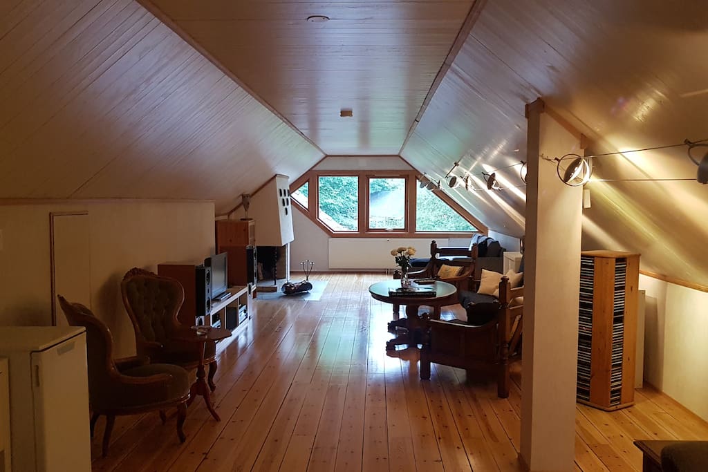 Romslig loftstue med stoler, bord og sofa. TV-benk med dekoder, forsterker, høyttalere og TV.