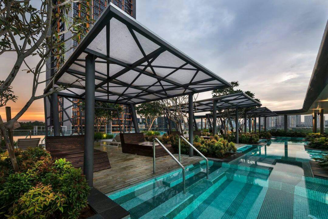 A rooftop area features a serene infinity pool surrounded by lush greenery and shaded seating areas. Modern architectural elements are highlighted by soft lighting as the sun sets in the background, creating a peaceful retreat for relaxation.