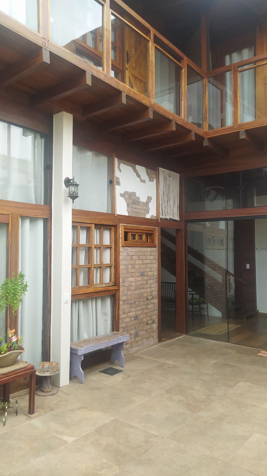 The interior space features a blend of warm wooden accents and large glass panels, allowing natural light to illuminate the area. A decorative wall piece is visible, alongside various textures created by brick and wood. A bench sits against the wall, enhancing the rustic charm.