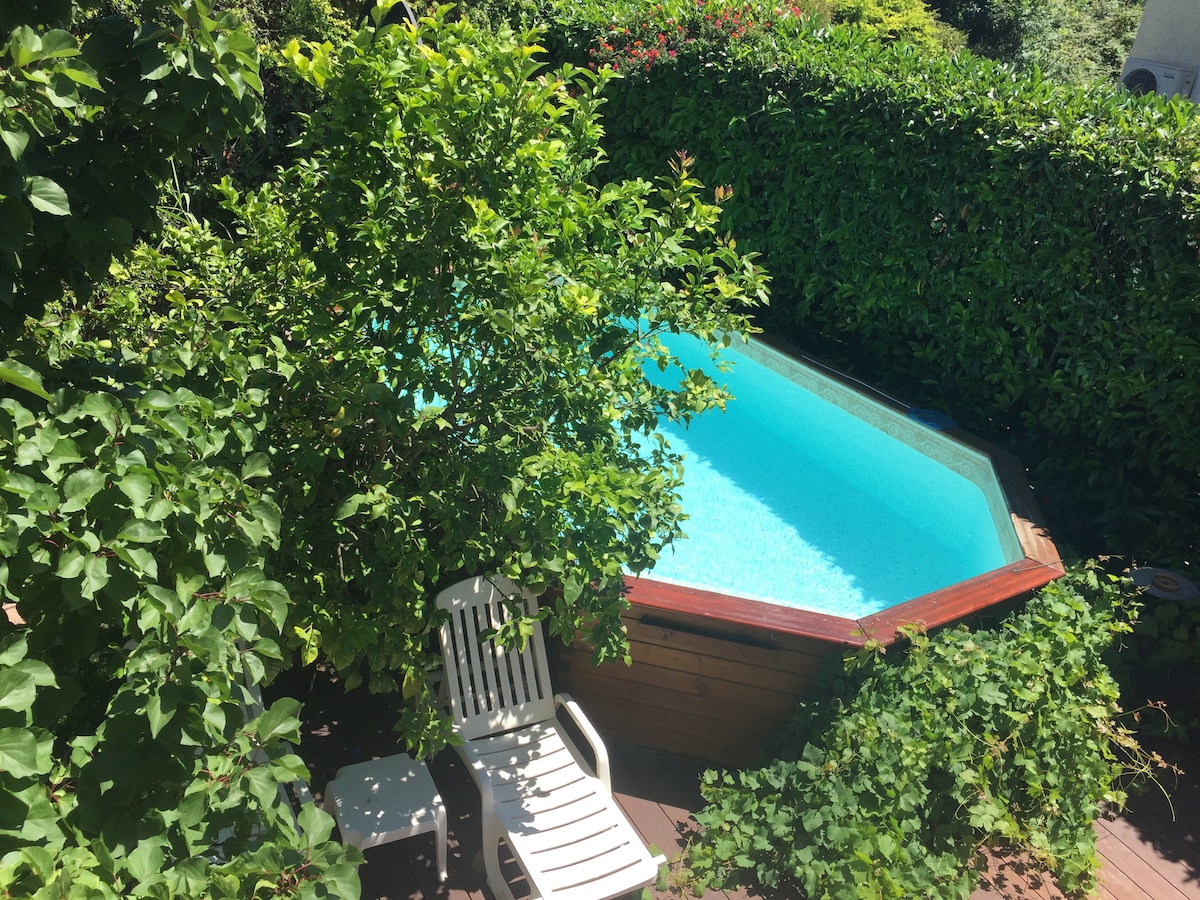 A private pool is surrounded by lush green foliage, providing a secluded retreat. A white lounge chair is positioned nearby on the wooden deck, emphasizing the tranquil setting. The clear blue water invites relaxation, while the abundant greenery enhances the sense of privacy.