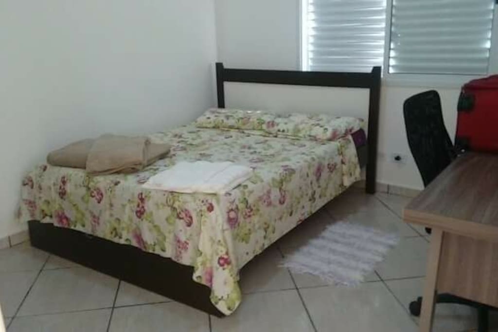 Cama de casal, nesse quarto tem uma escrivaninha e cadeira de escritório para trabalho estudos ou leitura