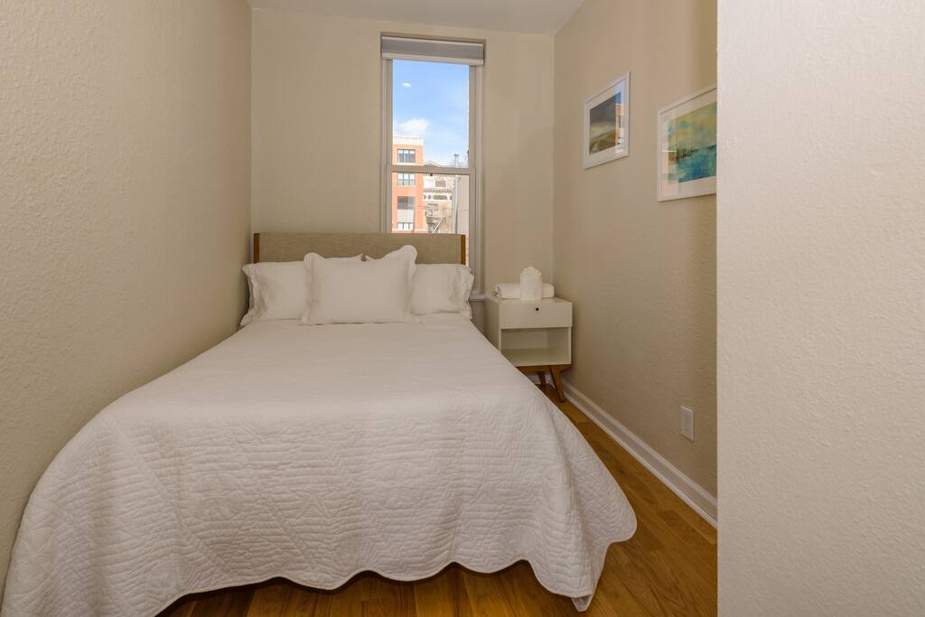 The cozy second bedroom has a double bed with a Leesa memory foam mattress, bedside table and city views.