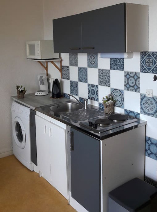 Coin cuisine avec lave-linge, deux plaques de cuisson électriques. En hauteur on retrouve le micro-onde en dessous, une bouilloire avec le plan de travail.