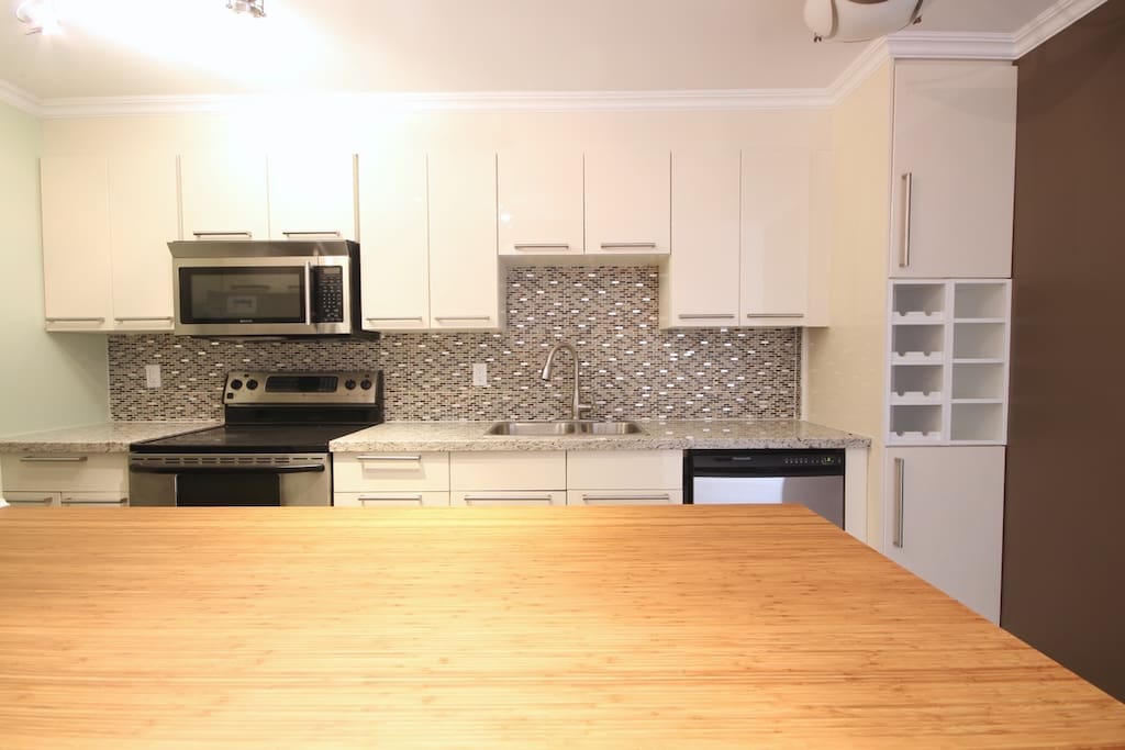 Kitchen with double oven, stove, dishwasher, microwave, granite counter top and bamboo island