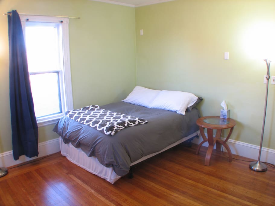 Full size bed, bedside table, and sunlit window