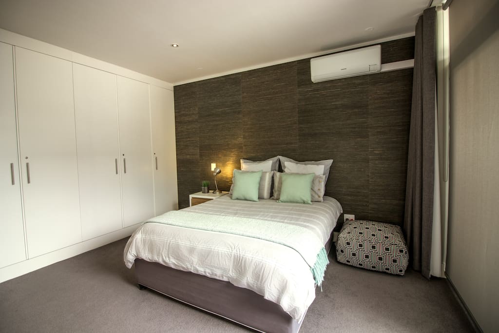 Modern, spacious bedroom with queen bed, air conditioner and cupboards