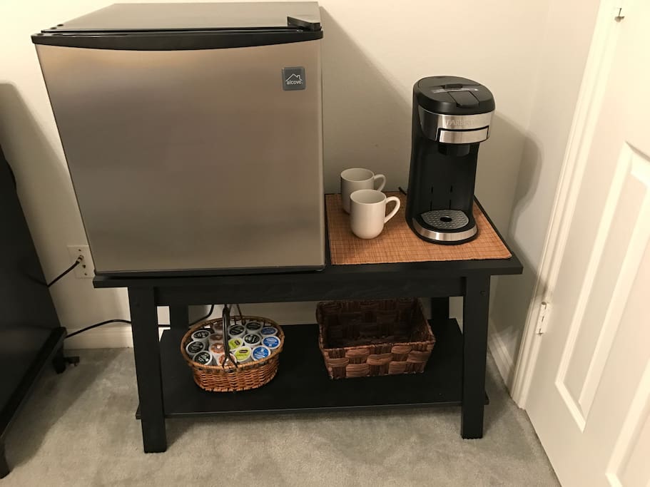 Fully stocked mini fridge in room with coffee maker, coffee and snacks.