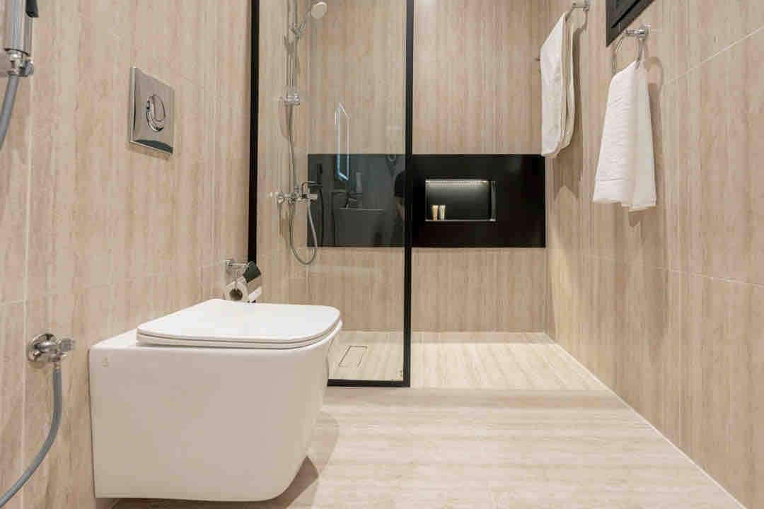 A modern bathroom features a walk-in shower enclosed by glass walls, emphasizing sleek design. A contemporary toilet is positioned to the side, accompanied by neatly arranged towels hanging on hooks. Soft lighting illuminates the space, creating a clean and inviting environment.