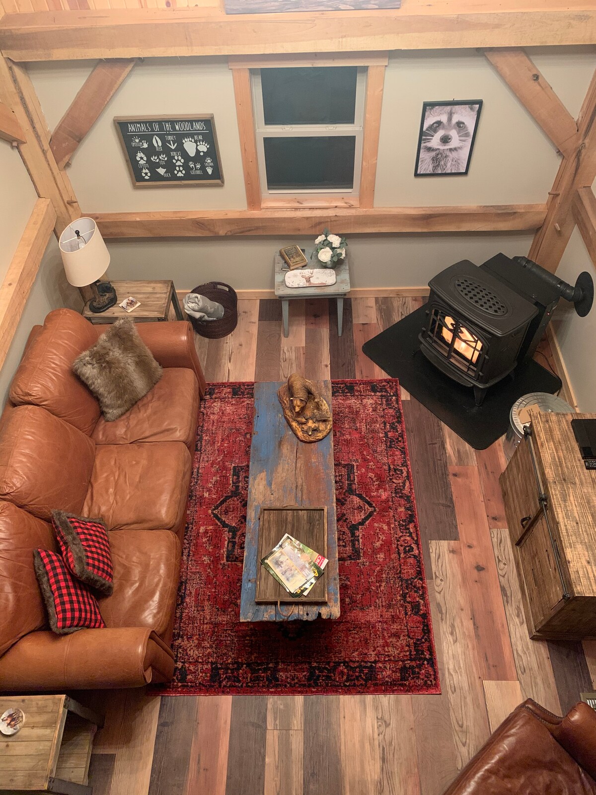 An overhead view of a cozy living area showcases a leather sofa alongside a rustic wood coffee table. A warm pellet stove is positioned nearby, with a decorative rug underfoot. Natural light filters through a window, enhancing the inviting atmosphere.