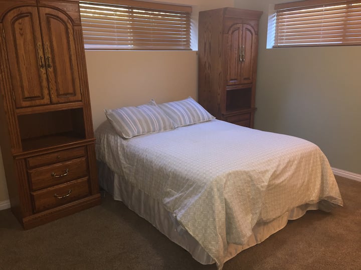 Bedroom #1 with full size bed. Lots of storage space, including closet space with hangers and laundry hamper.  Includes a desk and chair with lamp.  Light green/beige walls invite tranquility.