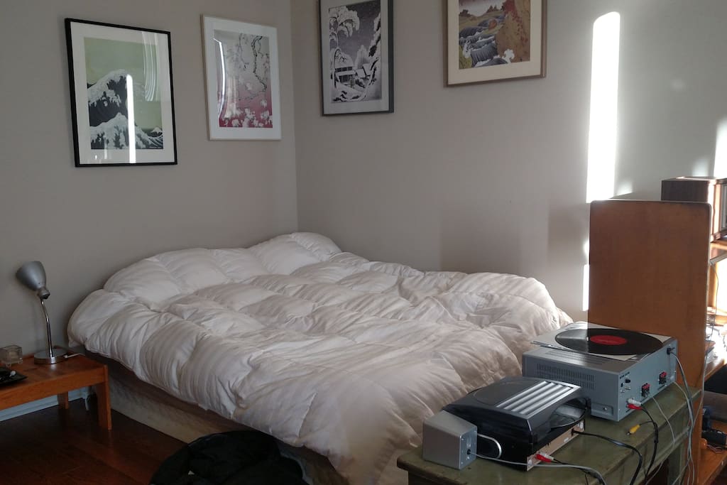 Main sleeping area with queen size bed, nightstand, record player, and prints by Kozyndan.