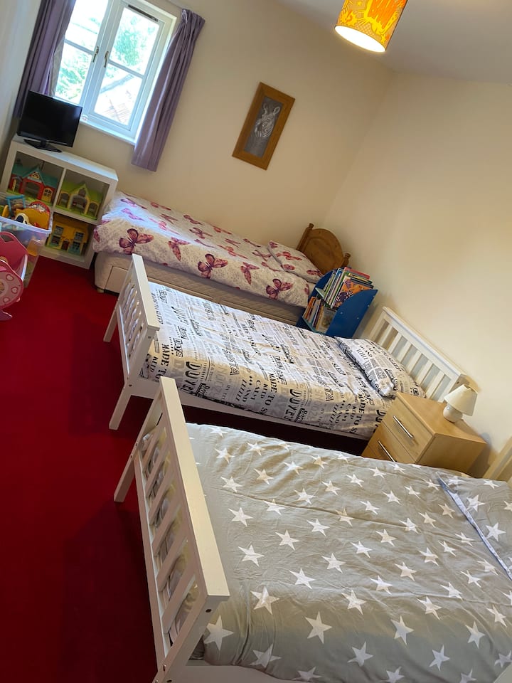 Трокреветна соба со три единечни кревета, погодна за деца или возрасни. Полица за книги со избор на детски книги и игри. Кутија за играчки и полици со згради на Happyland и луѓе. 