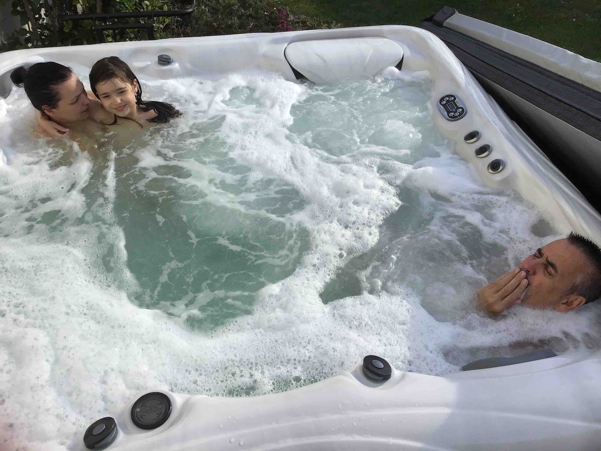 A spa with bubbling water is shown, providing space for relaxation. The surface is adorned with jets, and the surrounding area features lush greenery. The ambiance invites a sense of calm, ideal for unwinding after a day of activities.