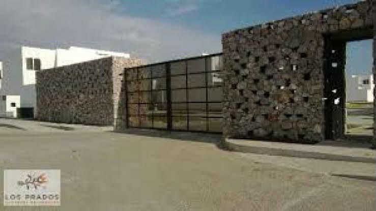 A modern entrance features a combination of stone walls and large glass panels, creating a striking contrast. The pathway is lined with smooth surfaces leading into the compound. Clear skies provide natural light that enhances the overall design of the entrance.