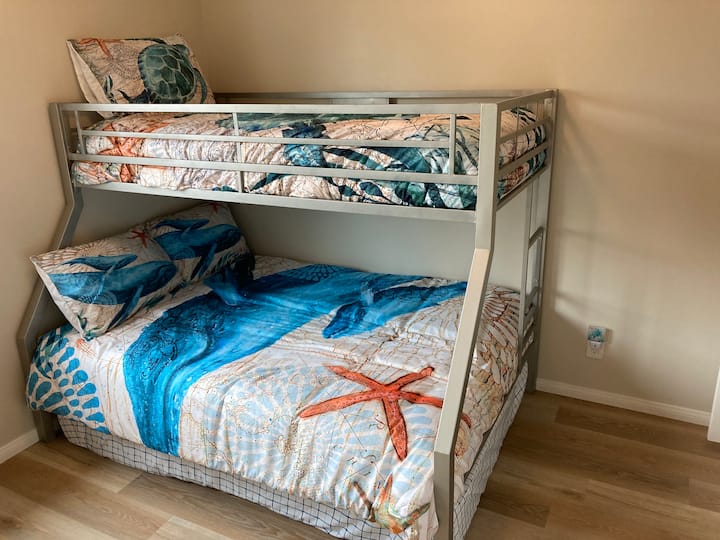 חזית: חדר שינה שני עם מיטה זוגית מעל מיטת קומתיים מלאה. מזרן מיטה מלא נוסף שאפשר להחליק מתחת.