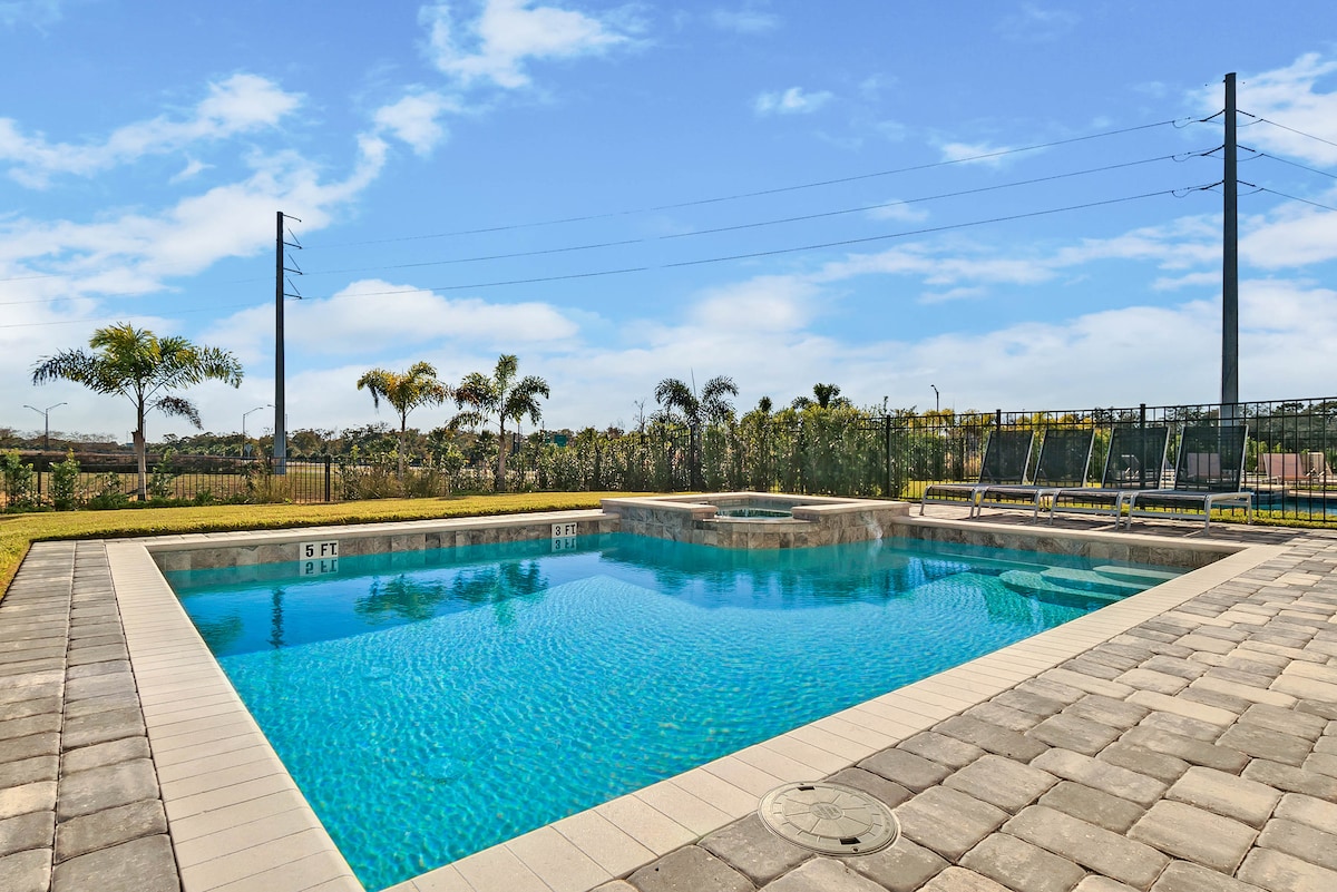 A private pool is surrounded by a paved deck, featuring clear water that reflects the blue sky above. Lush greenery borders the area, providing a sense of tranquility. A child safety pool fence encircles the pool, enhancing safety for younger guests.