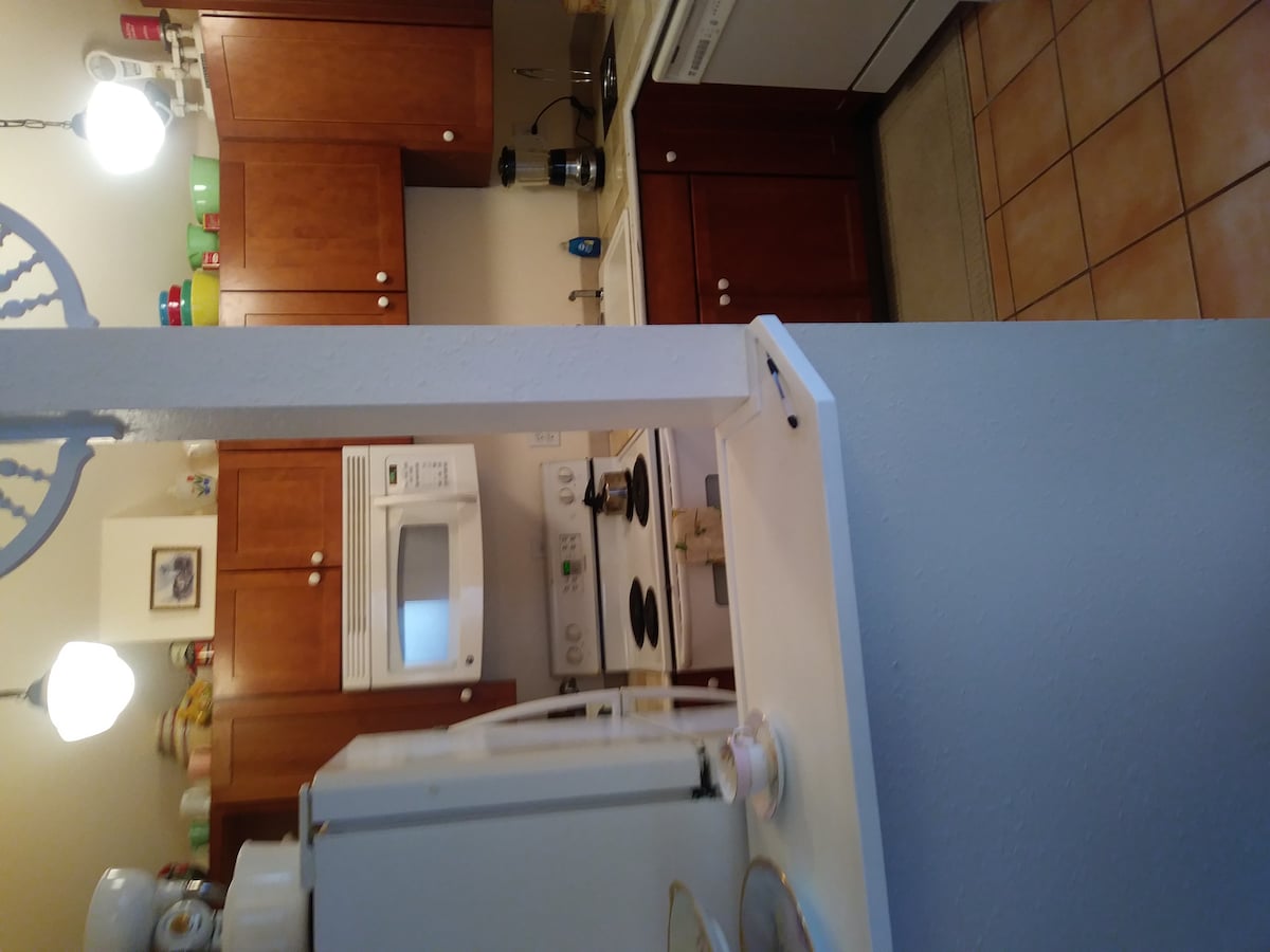 A well-equipped kitchen features warm wooden cabinetry and a countertop view. Appliances include a microwave, stove, and dishwasher. Light-colored tiles cover the floor, and overhead lighting illuminates the space. The area appears functional and inviting for meal preparation.