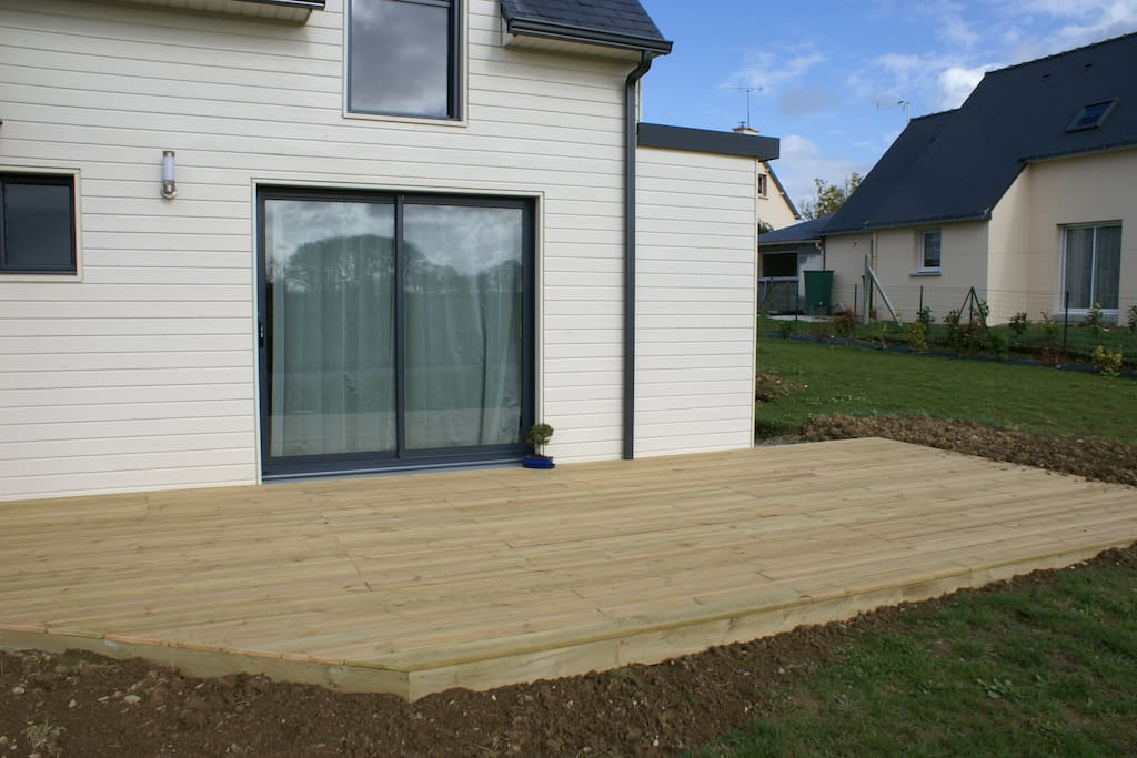 maison en bois, terrasse terminée. Pelouse tout autour, balançoire et cabanons pour enfants et adultes