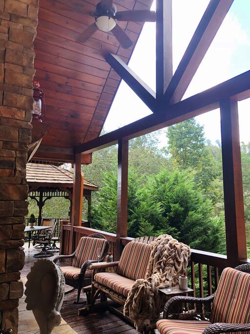 Covered top balcony with seating area around wood burning fireplace & gas grill with views of the river