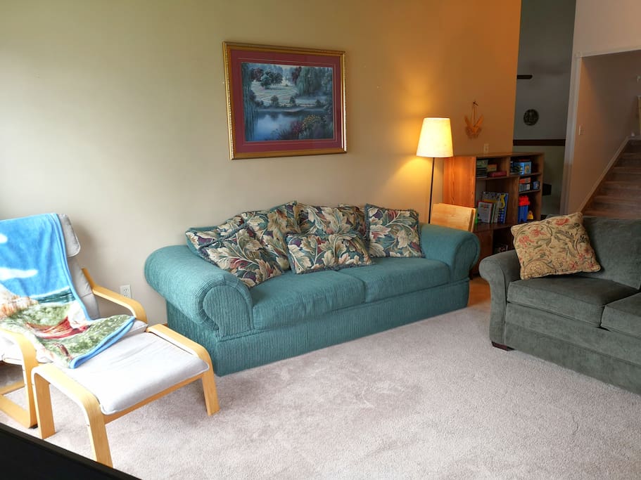 LIVING ROOM - 2 full sized couches, chair & ottoman, and entertainment cabinet, with a view to the dining room and short stairway to the bedrooms & bathroom on the upper level