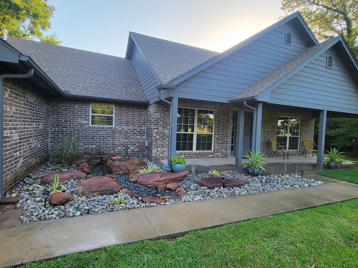 The front exterior of the home features a stone pathway leading to a covered porch area, surrounded by landscaped beds with decorative rocks and plants. Large windows allow for natural light, while a well-maintained lawn enhances the welcoming entrance.