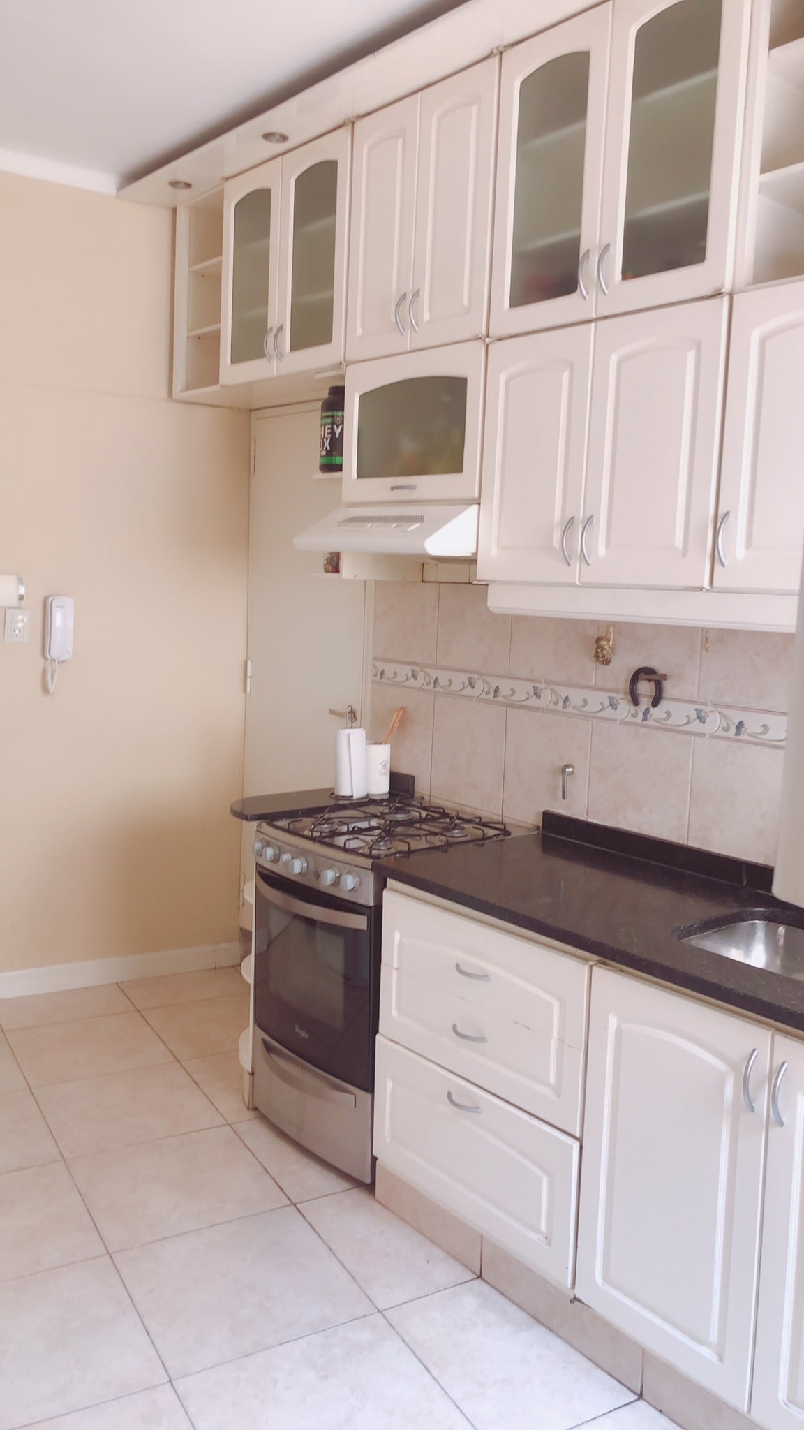 A functional kitchen space features white cabinetry and a dark countertop. The gas stove is positioned on the left, accompanied by an overhead microwave. A small sink is located to the right, with a tile backsplash providing a simple accent.